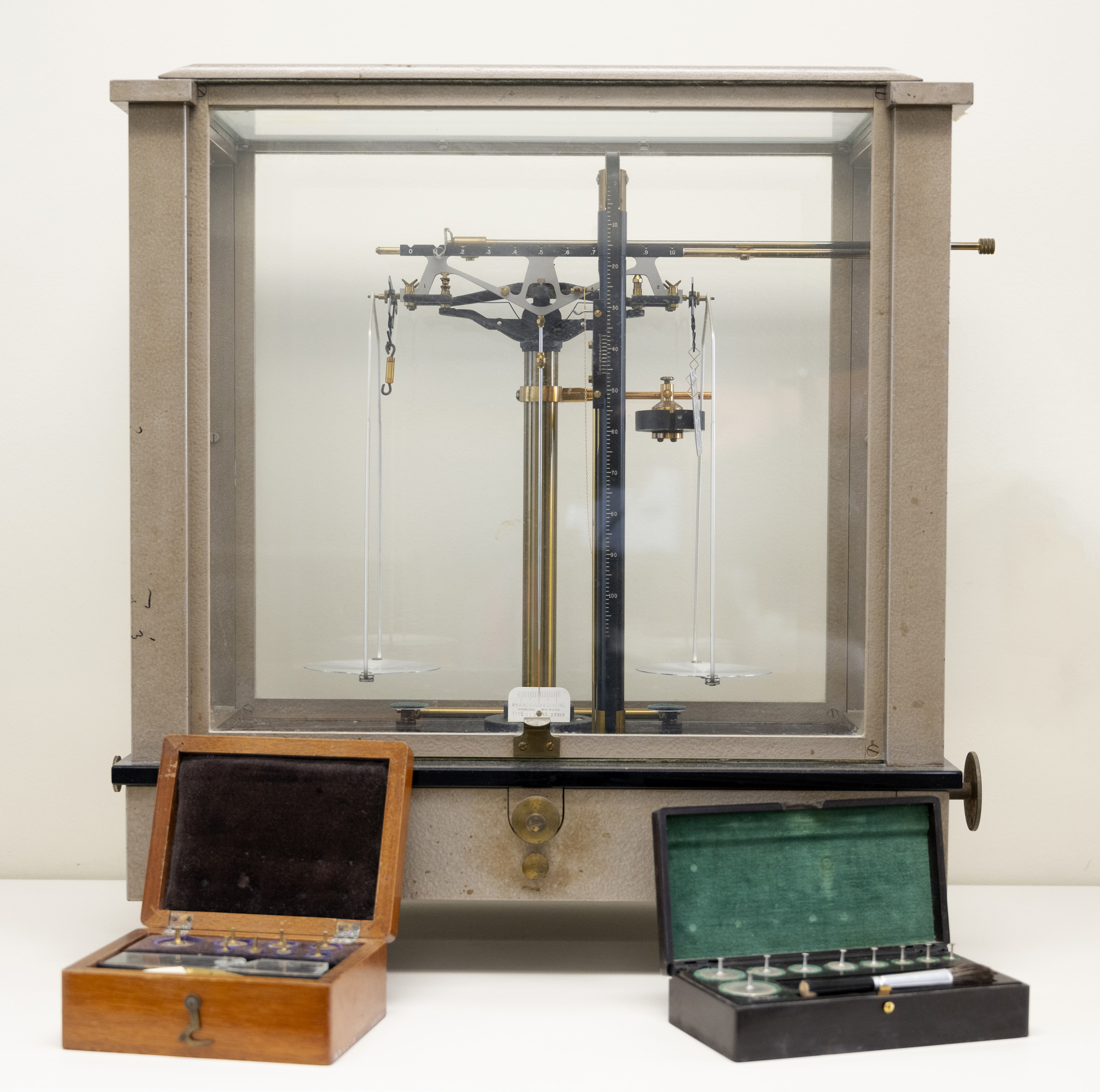 Set of scales in a glass and metal case with two small boxes of weights in front.