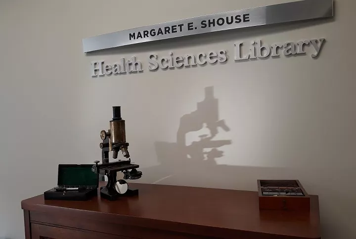 Antique microscope under a sign for the Shouse Health Sciences Library