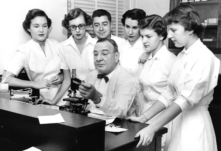 Doctor at a microscope surrounded by students